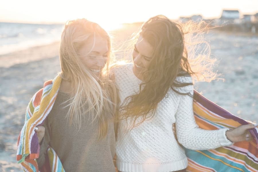 Two girls on the beach with a colorful towel around them.