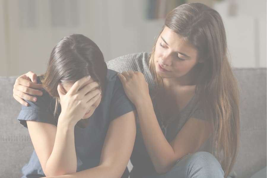 Two girls consoling one another on a couch.