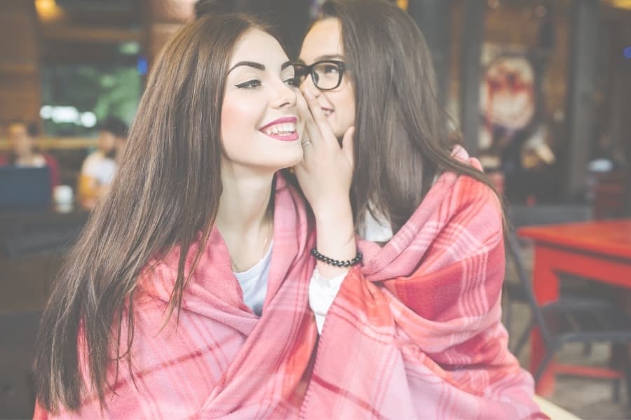 Two girls wrapped in a pink blanket sharing secrets.