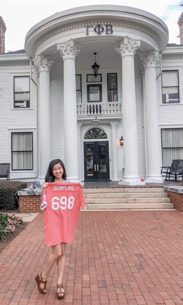 Juliet Meiling holding her sorority jersey up in front of the Gamma Phi Beta sorority house at the University of Georgia.