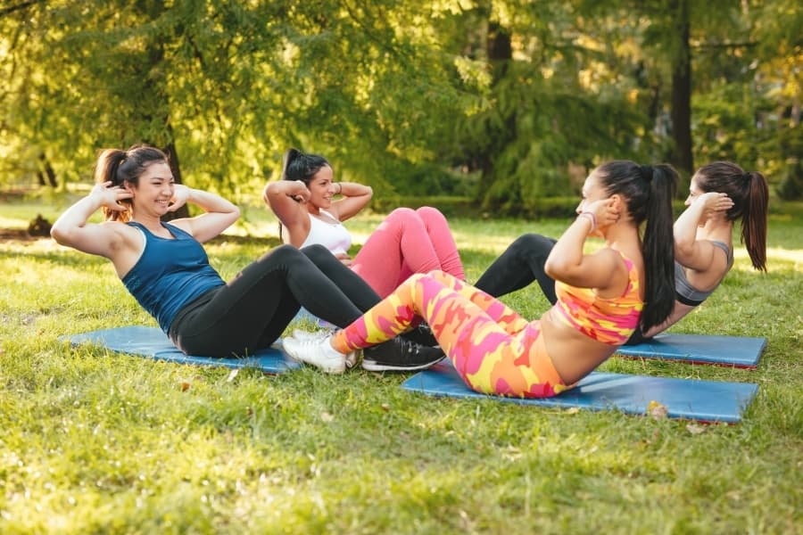 Four women working out together outside at a park to make friends after graduating from college.